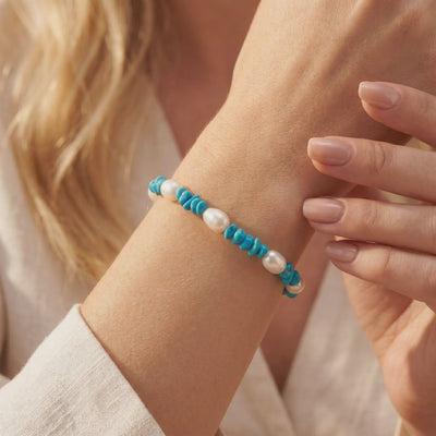 Turquoise and white freshwater pearl bead bracelet worn on a wrist in a warm-lit close-up.