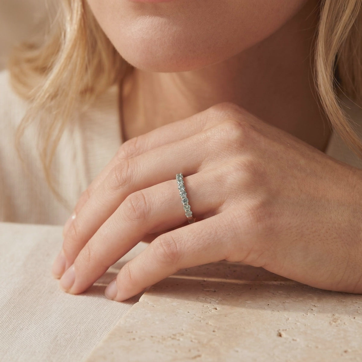 Silver eternity ring with pale green round stones worn on a woman's ring finger.