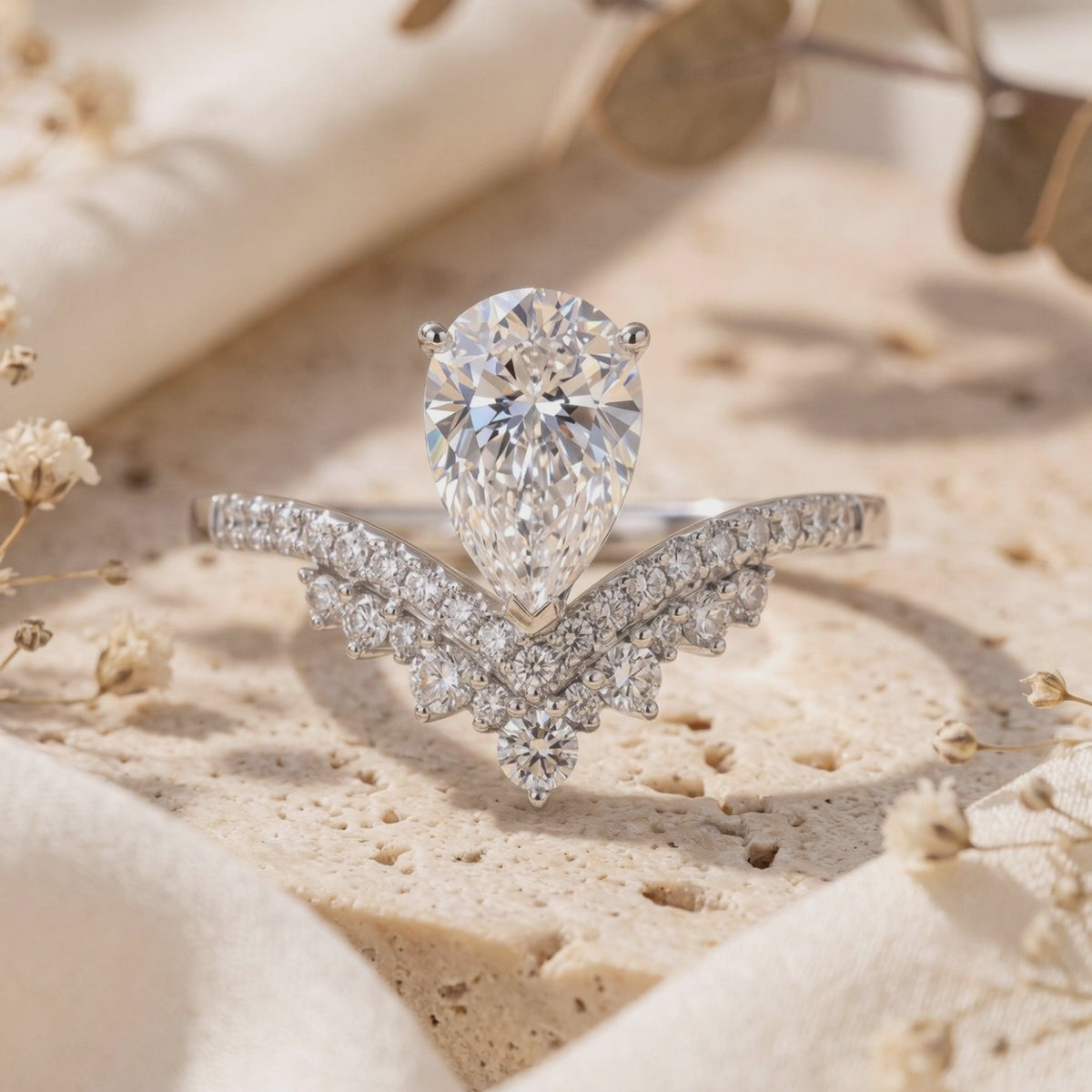 Upright silver wishbone ring with a pear-cut center stone and layered pavé bands on a textured stone surface.