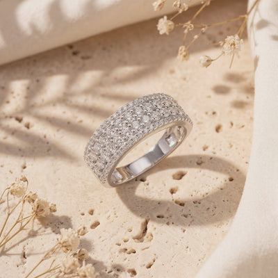 Wide silver multi-row cubic zirconia ring displayed at an angle on a textured stone surface.