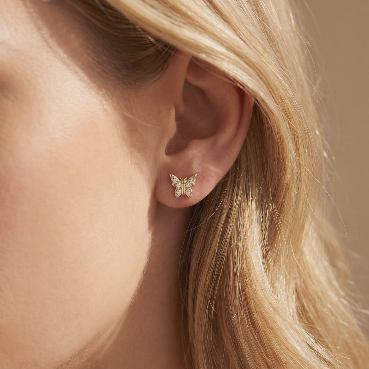 Gold-toned butterfly stud earring with round stones worn on an earlobe, shown in close-up.