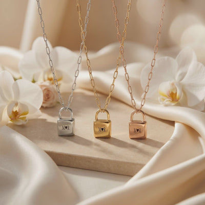 Three engraved padlock pendant necklaces in silver, gold, and rose-gold tones displayed on draped fabric.