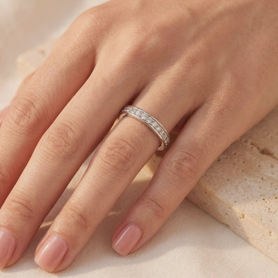 Silver cubic zirconia eternity ring worn on a hand against a soft neutral backdrop.