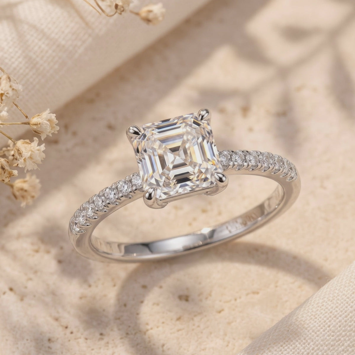 Close-up of the silver ring on textured fabric, showing its square center stone and pavé-set band beside dried flowers.