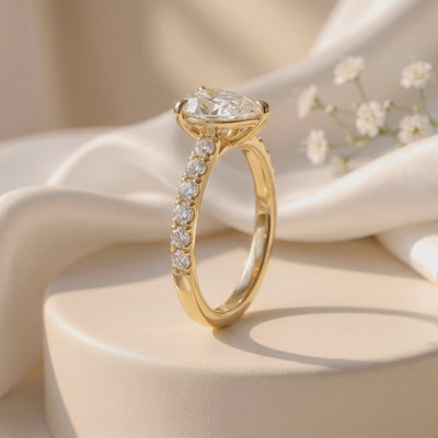 Side view of a gold-tone pear-cut pavé solitaire ring displayed upright on a cream pedestal with white fabric.