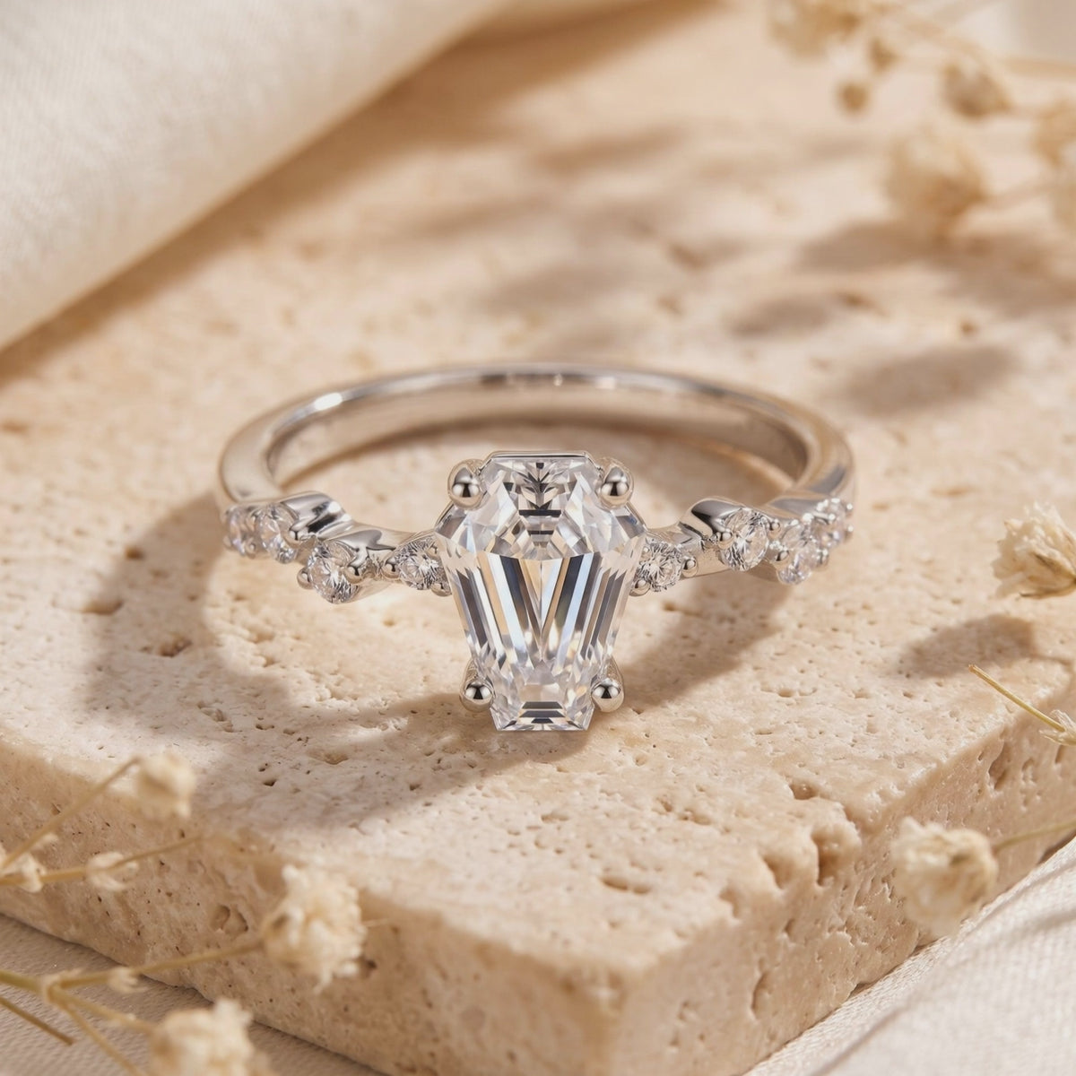 Close-up of a silver ring with a coffin-cut clear center stone and accent stones, displayed upright on a stone surface.