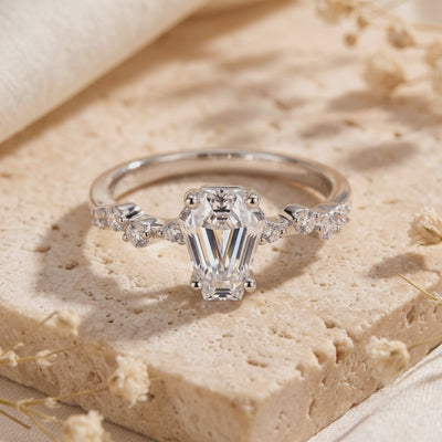 Close-up of a silver ring with a coffin-cut clear center stone and accent stones, displayed upright on a stone surface.