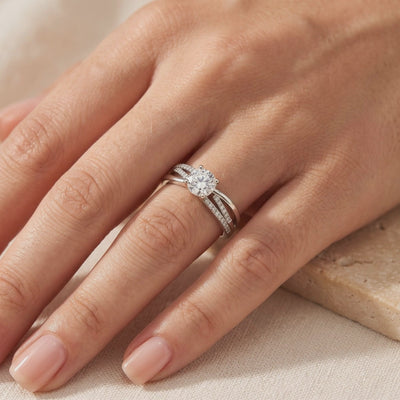 Silver crossover ring with a round center stone and accent-lined bands, worn on a hand.