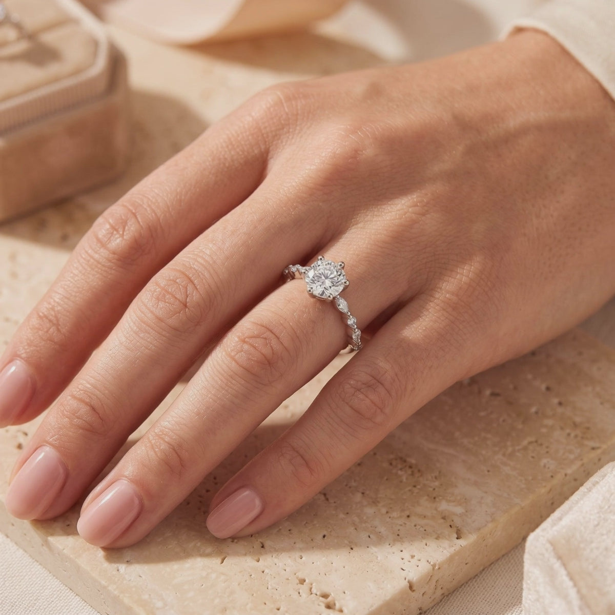 Silver ring with a round center stone worn on a hand against a neutral travertine block.