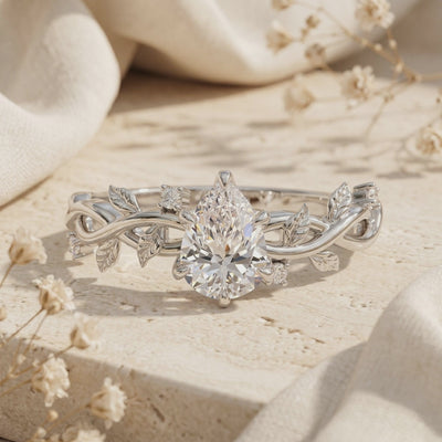 Macro view of pear-cut moissanite ring featuring a detailed silver leaf vine band.