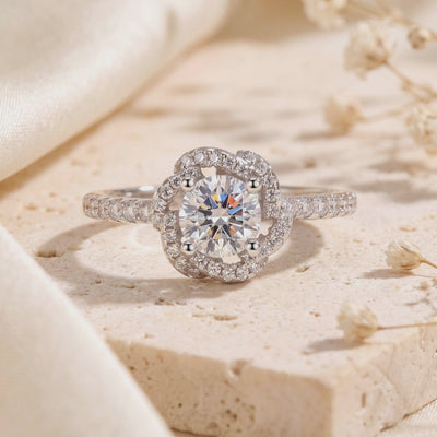 Close-up silver Rosette Swirl Halo ring with a round four-prong center stone resting on a textured stone surface.