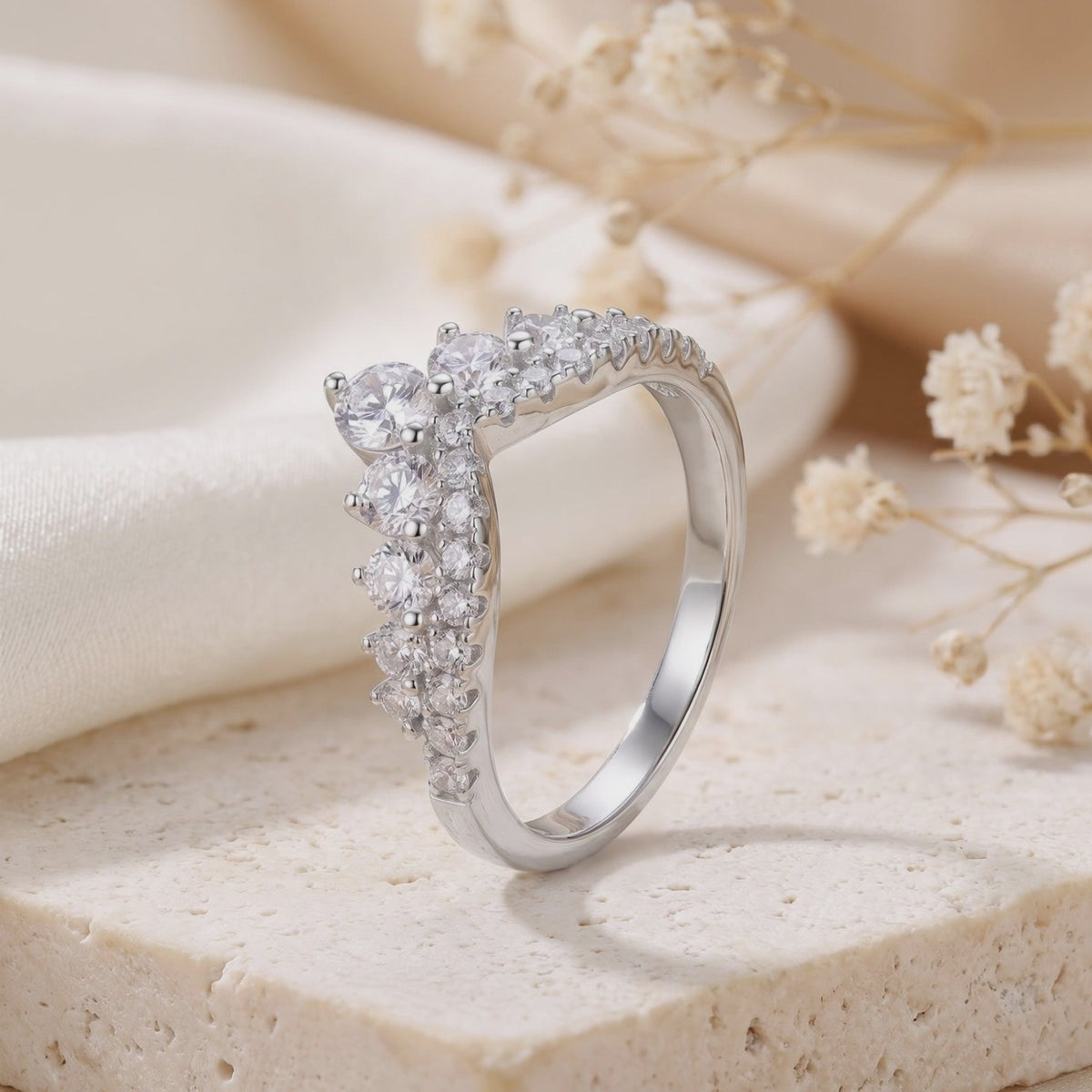 Close-up side view of a silver double-row chevron ring with clear cubic zirconia on a pale textured slab.
