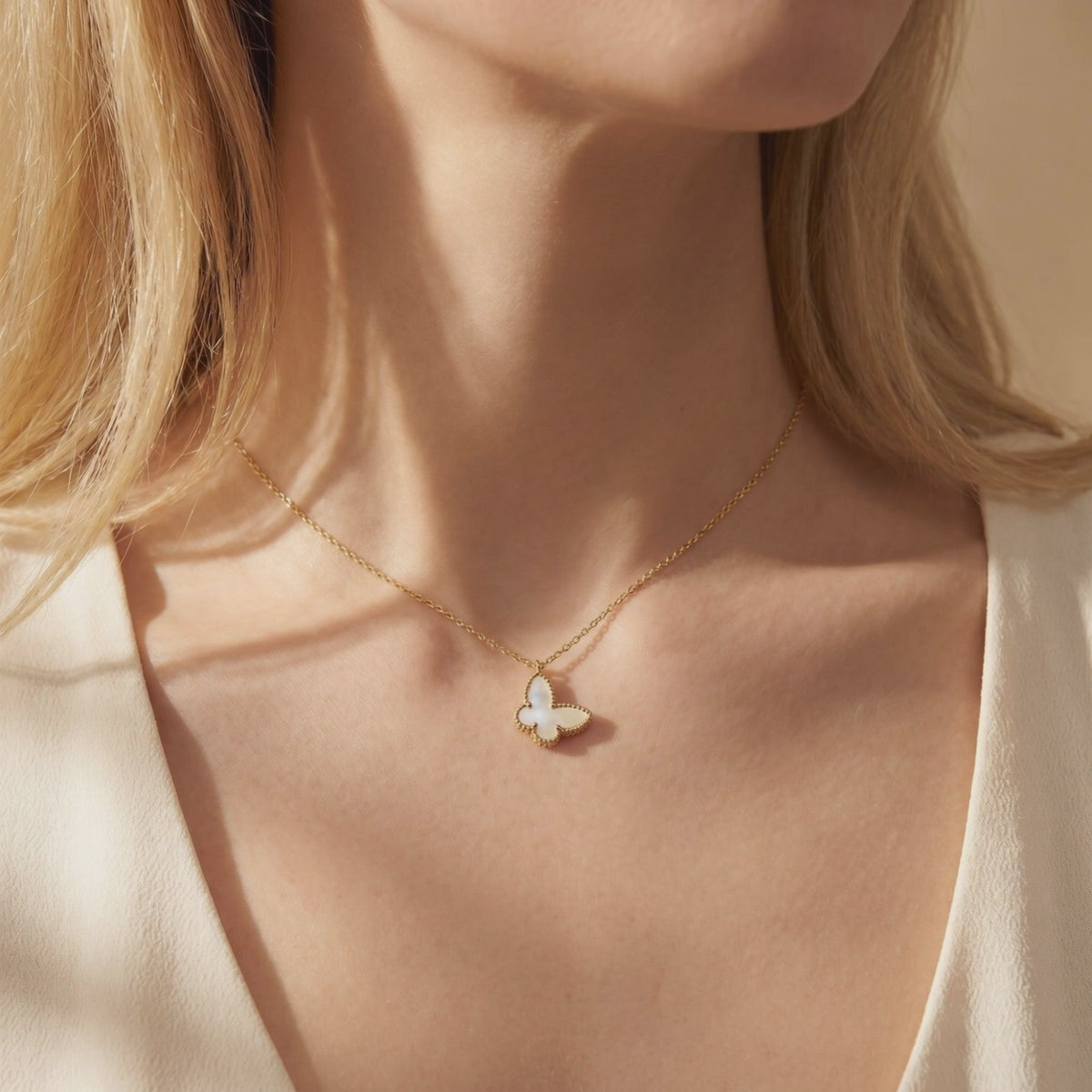 Mother-of-pearl butterfly pendant on a gold chain worn around a woman's neck.