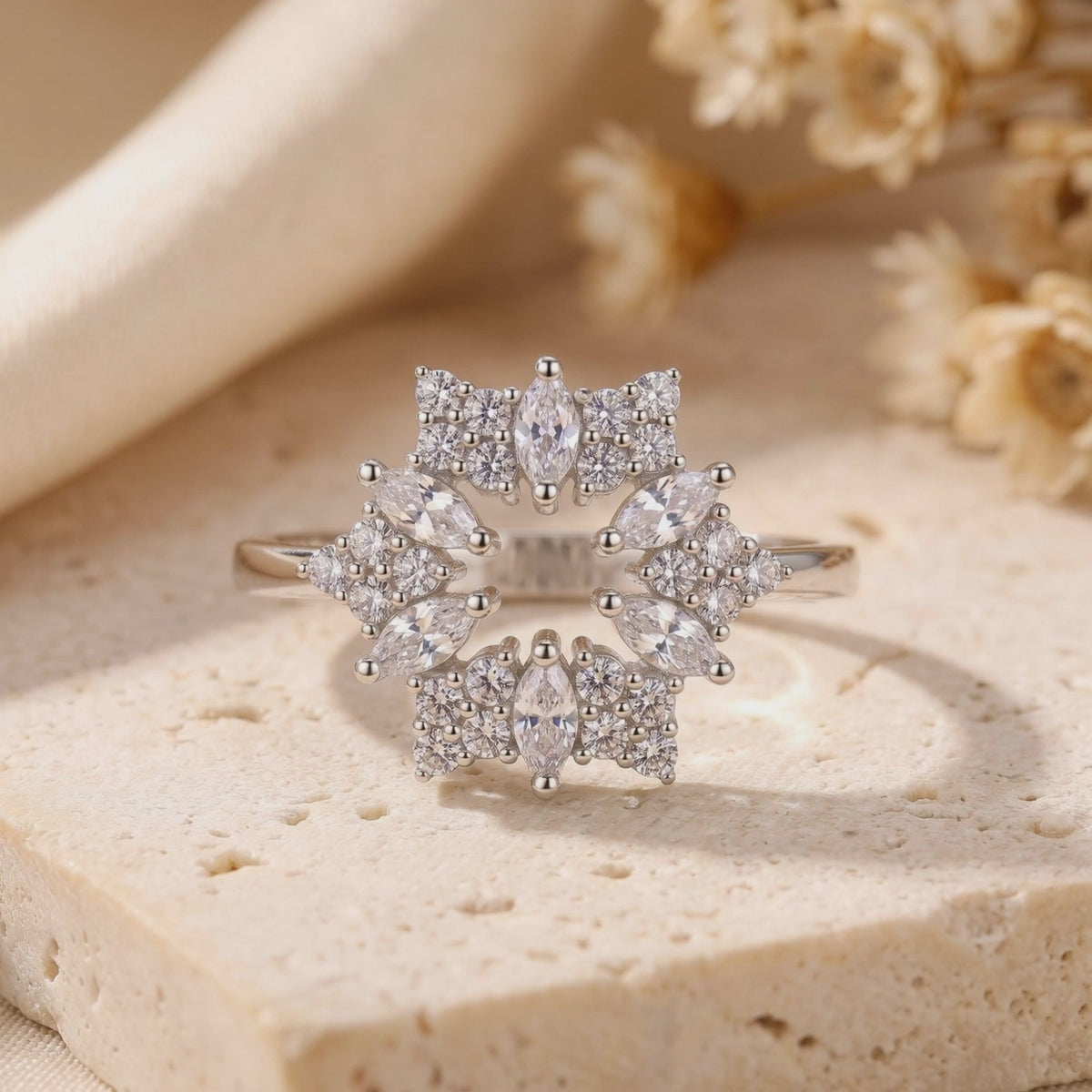 Close-up of the silver starburst ring standing upright on a beige stone surface.