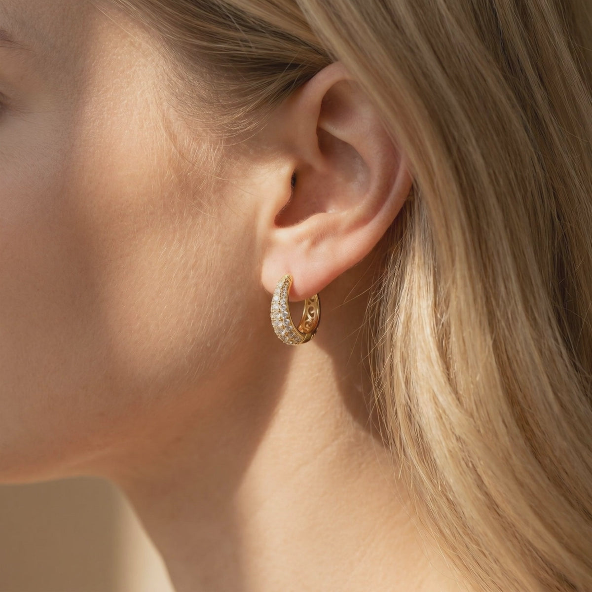 Model wearing a gold-tone J-hoop earring with multiple rows of round moissanite stones.