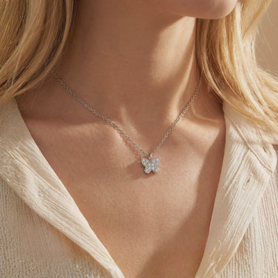 Silver-tone butterfly pendant with round clear stones on a fine chain, worn at a woman's collarbone.