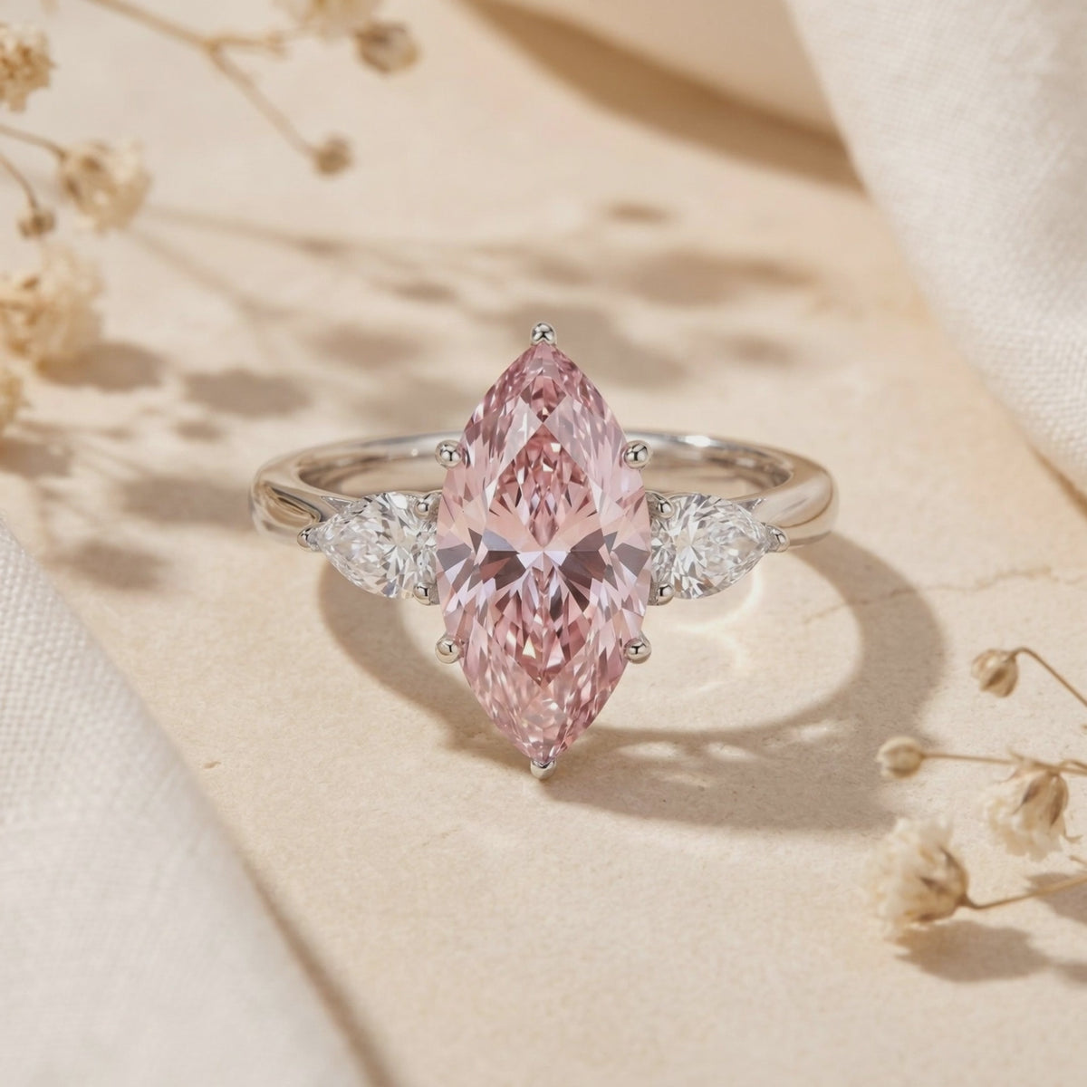 Video preview of a silver three-stone ring with a pink marquise center stone, upright on a beige surface.