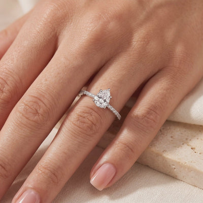Pear-cut clear stone ring with a pavé band, shown worn on a hand.