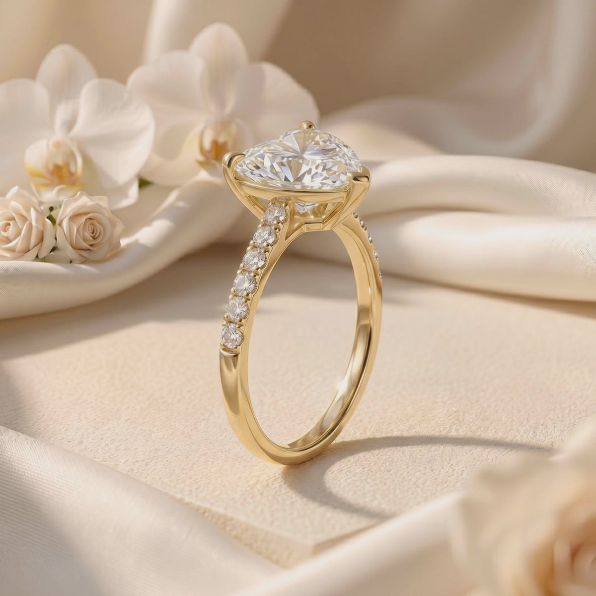 Three-quarter view of a yellow gold-tone heart-cut solitaire ring with pavé stones standing on white fabric.