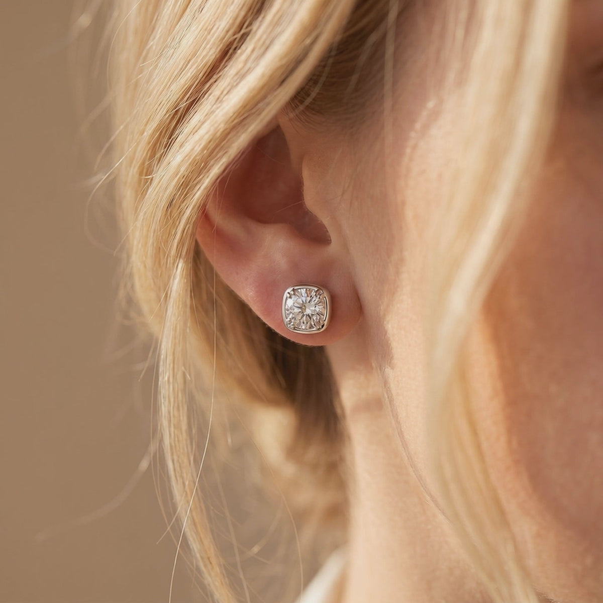 Close-up of a silver cushion-halo moissanite stud earring worn on an ear.