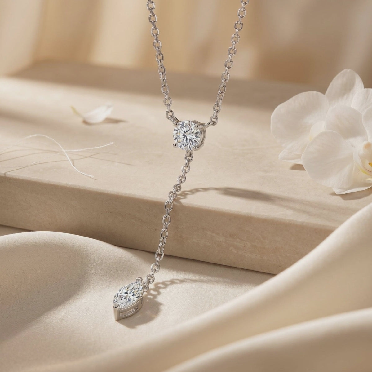 Close-up of a silver-tone moissanite lariat necklace on beige fabric, showing its round junction stone and marquise drop.