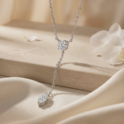 Close-up of a silver-tone moissanite lariat necklace on beige fabric, showing its round junction stone and marquise drop.