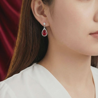Side view of a woman wearing a solid white gold teardrop earring with a red simulated ruby center stone and clear pavé halo.