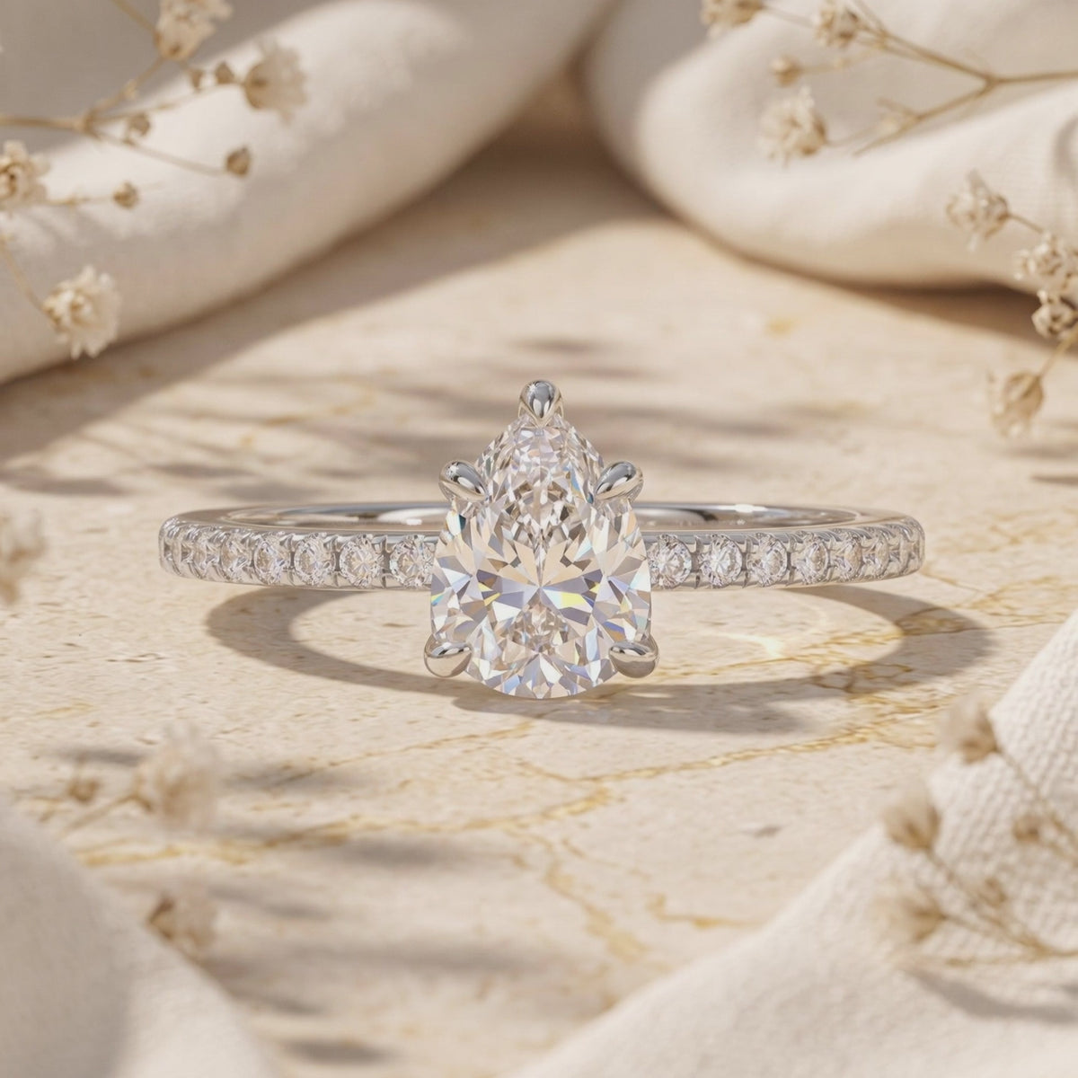 Close-up of a pear-shaped clear stone ring with a five-prong setting on a pavé band.