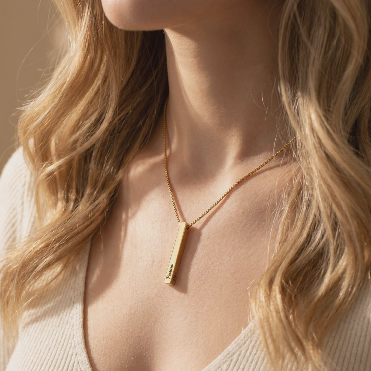 Gold-toned bar pendant necklace worn on a model’s neck, with dark engraved text on the pendant.