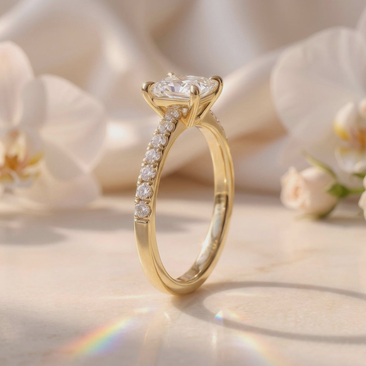 Side profile of a gold-tone princess-cut solitaire ring showing its prong setting and pavé band.