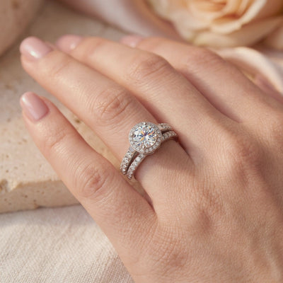 Silver halo ring set with a round center stone and pavé bands worn on a hand's ring finger.