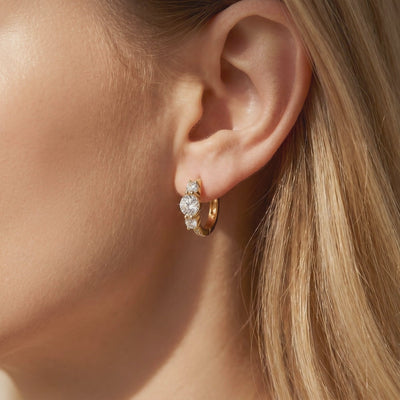 Close-up view of a gold-tone three-stone hoop earring worn on an earlobe.