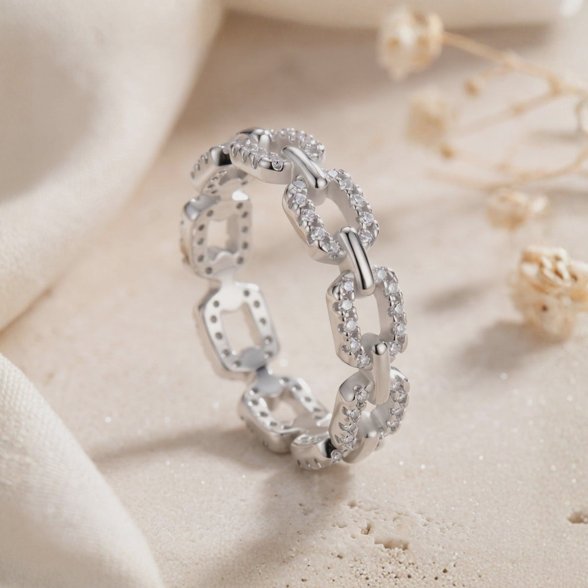 Close-up of a pavé chain-link ring standing on a light textured surface