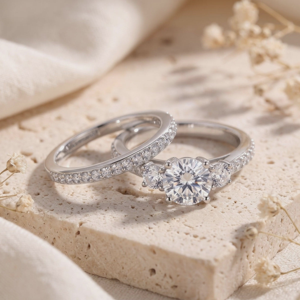 Silver three-stone ring and matching pavé band arranged on a beige stone block.