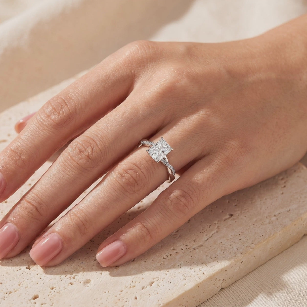 Radiant-cut clear stone ring with a twisted pavé band, worn on a hand.
