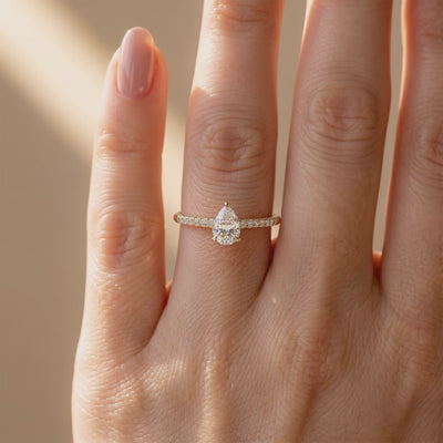 Pear-cut pavé solitaire ring worn on a finger in a close front view.