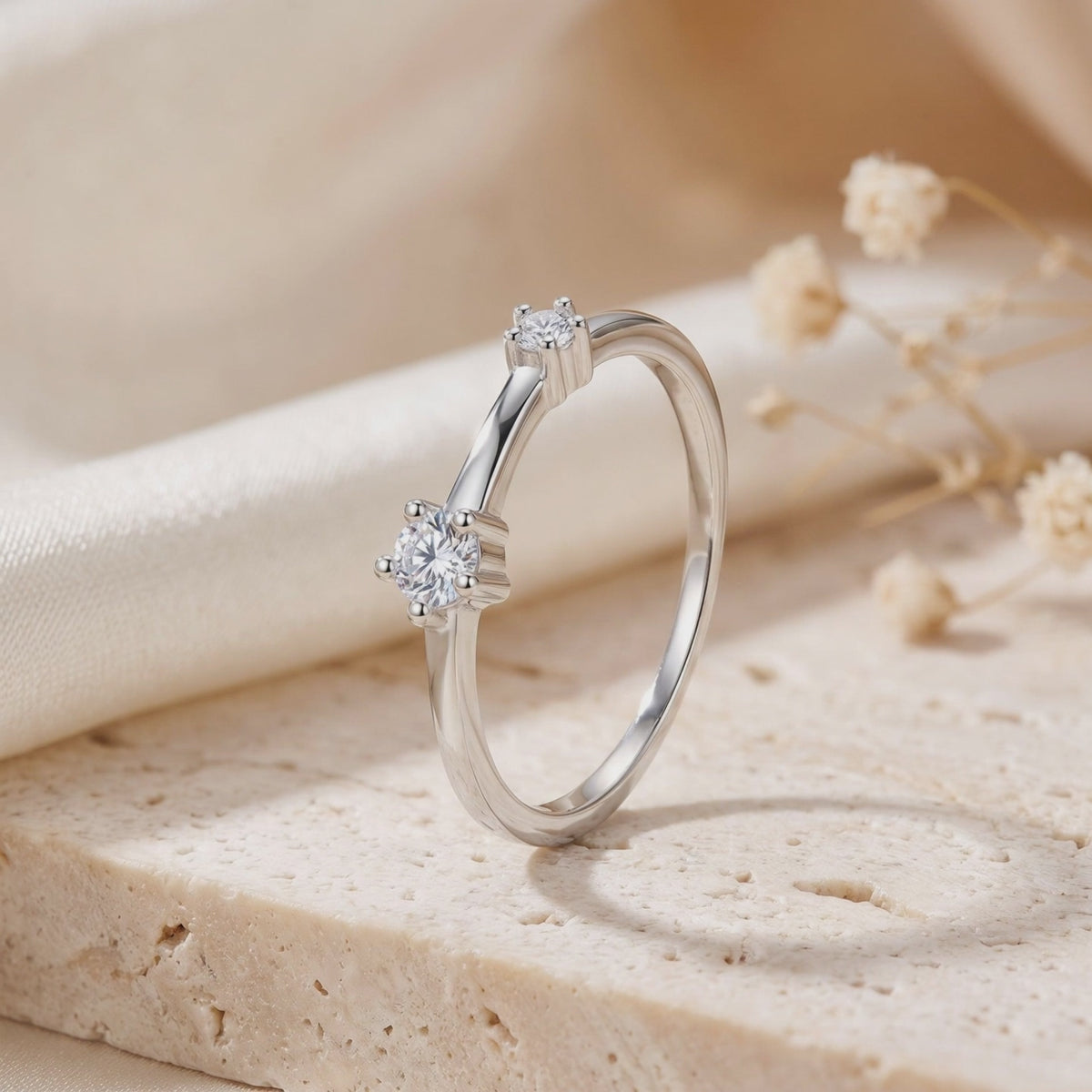 Silver asymmetric bypass ring with two clear stones, standing upright on a light textured slab.