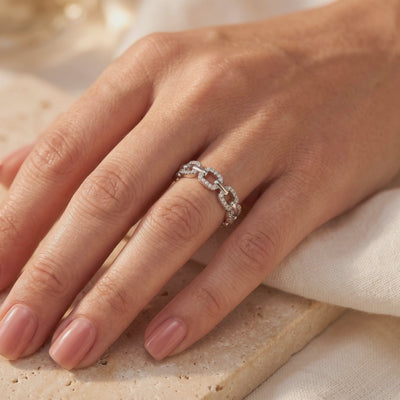 Pavé chain-link ring worn on a finger over a beige stone tile