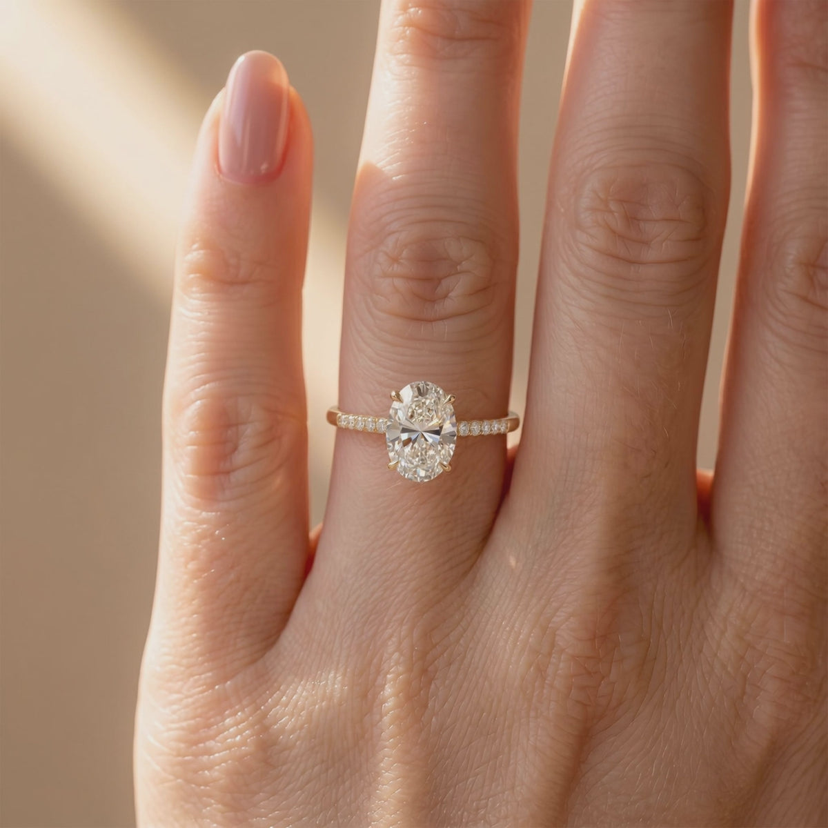 Ring worn on a finger, with an oval clear center stone and pavé-set band in a gold-colored finish.