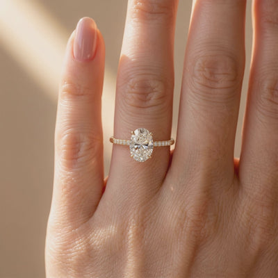 Ring worn on a finger, with an oval clear center stone and pavé-set band in a gold-colored finish.