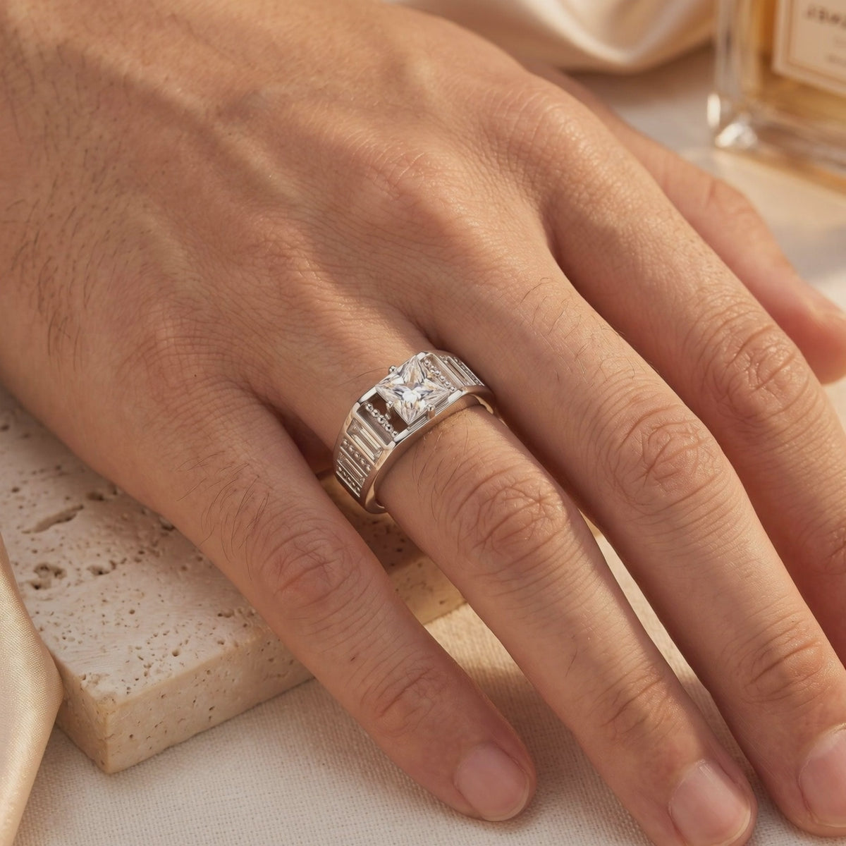 Silver ring with a princess-cut simulated diamond worn on a hand over travertine and silk fabric.
