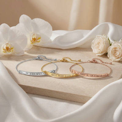 Three bar bracelets in silver, gold, and rose gold tones displayed on stone with white flowers.