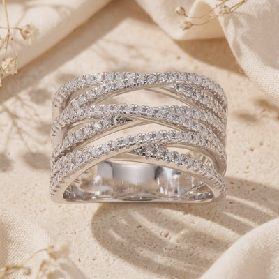 Upright silver multi-row criss-cross pavé ring shown on a textured beige surface, with the open interior visible.