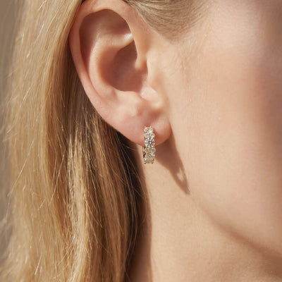Close-up of a gold-tone hoop earring with round moissanites worn on an earlobe.