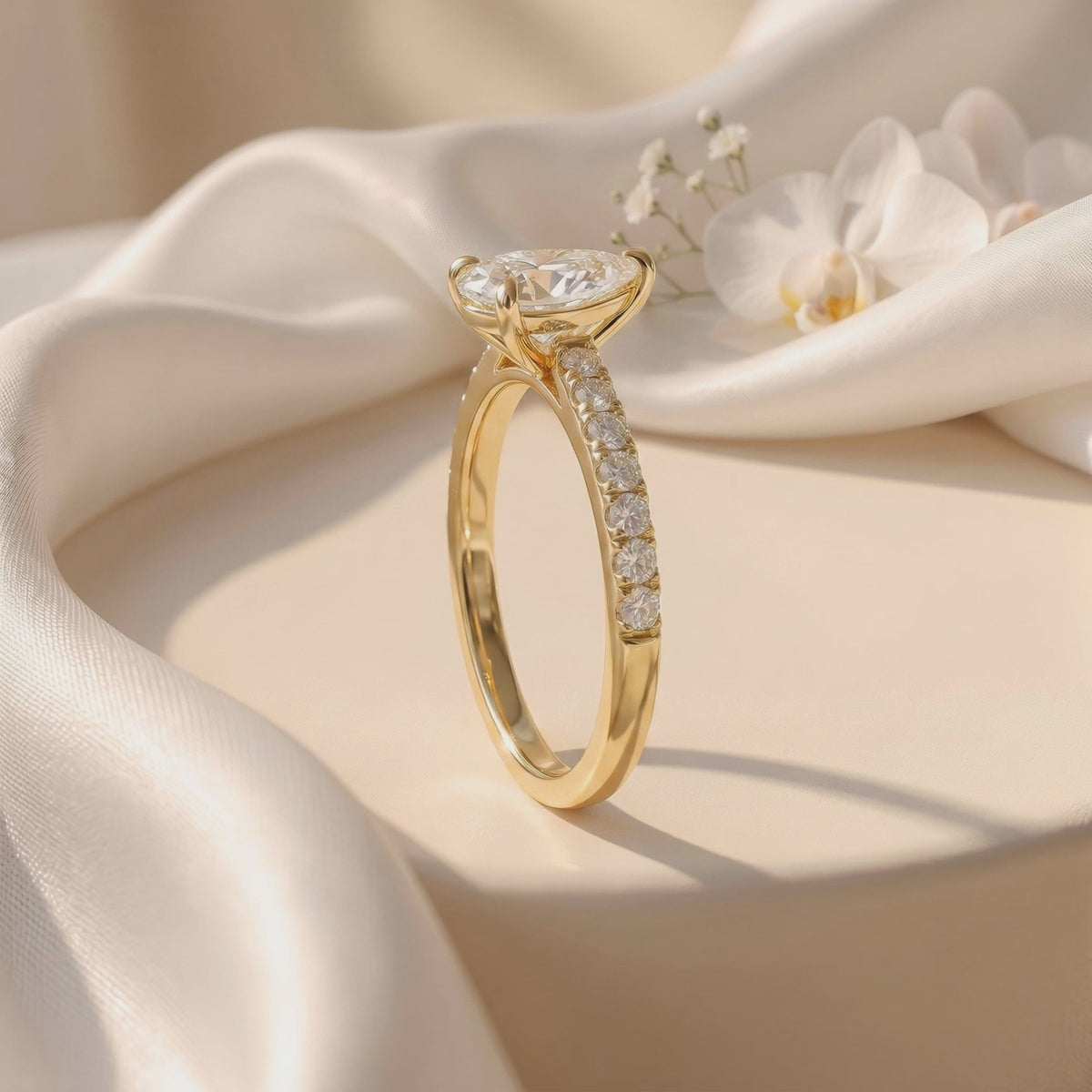 Pear-cut pavé solitaire ring standing upright on draped white fabric, showing its raised setting and pavé side.