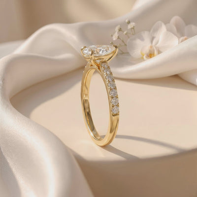 Pear-cut pavé solitaire ring standing upright on draped white fabric, showing its raised setting and pavé side.