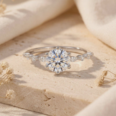 Close-up of a silver ring with a six-prong round stone and marquise band accents on textured stone.