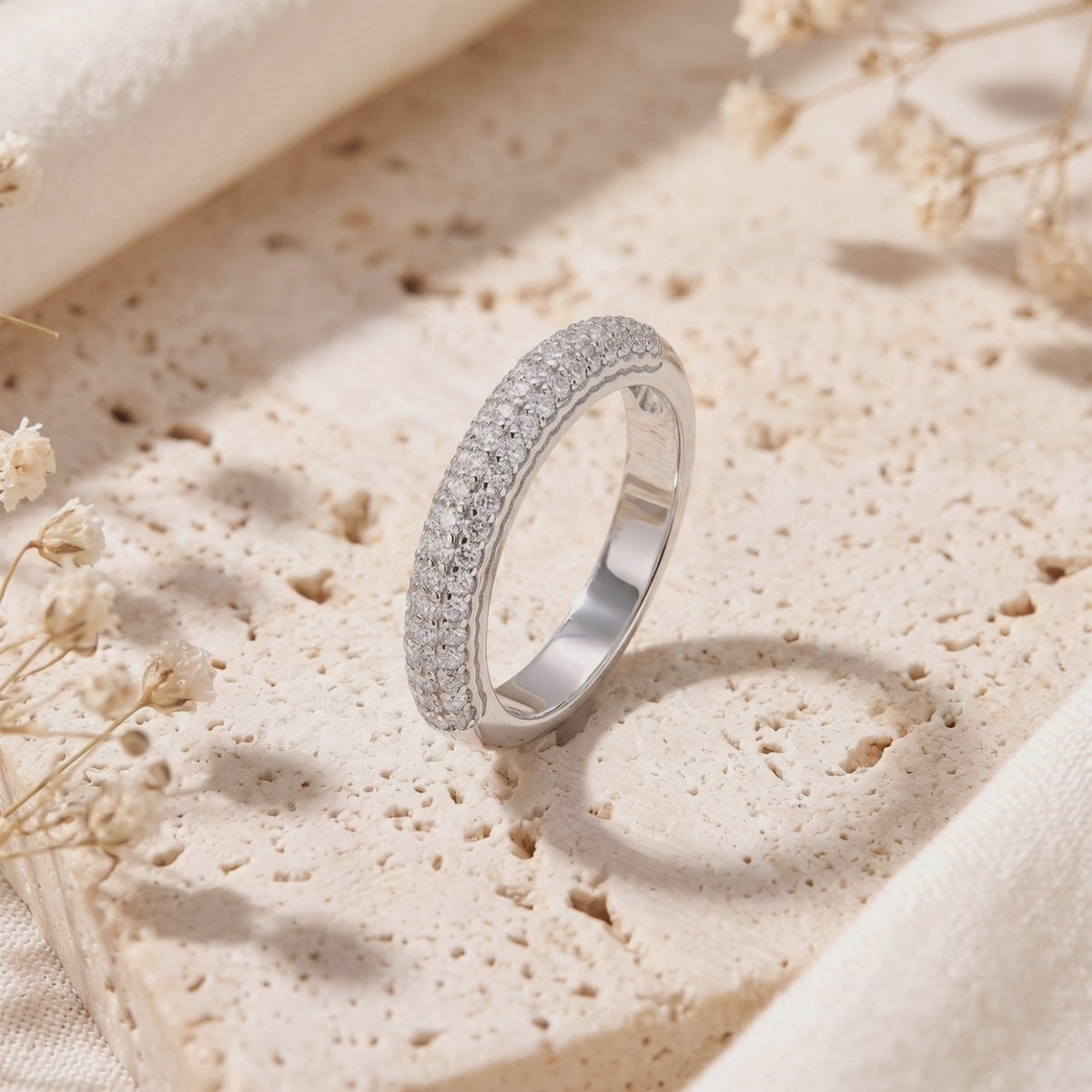 Silver triple-row pavé band standing upright on a porous beige stone surface, showing its polished inner band.