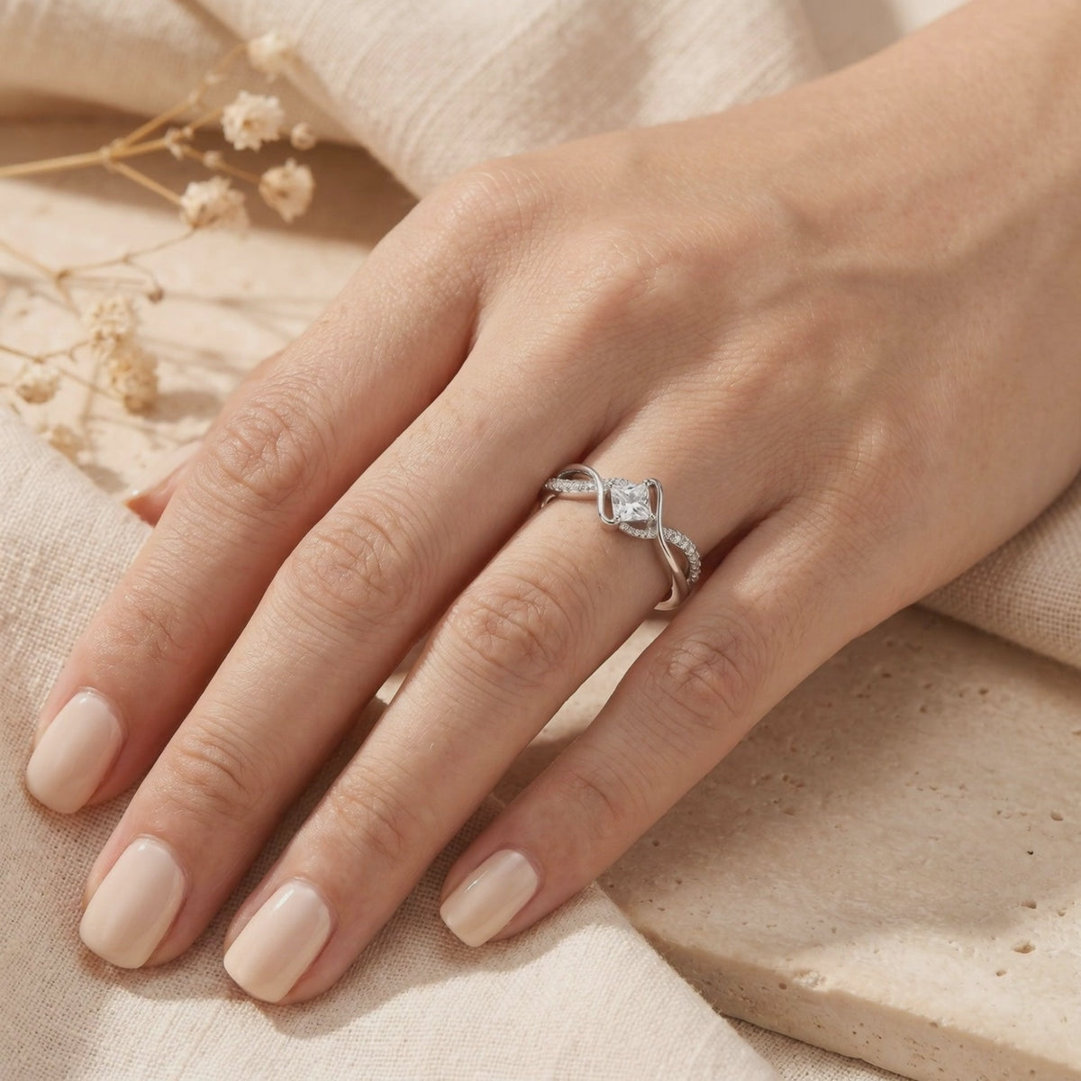 The silver princess-cut moissanite ring with a twisted band worn on a hand against a neutral background.