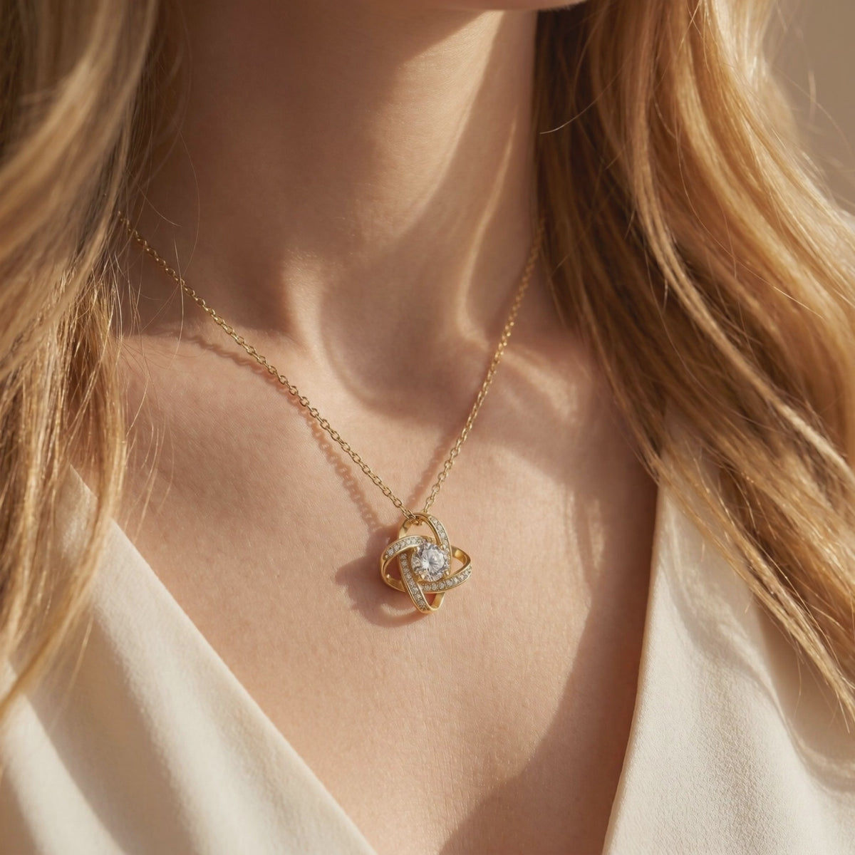 Gold-toned interlocking knot necklace with a clear center stone, shown in a close-up while worn on a person's neck.